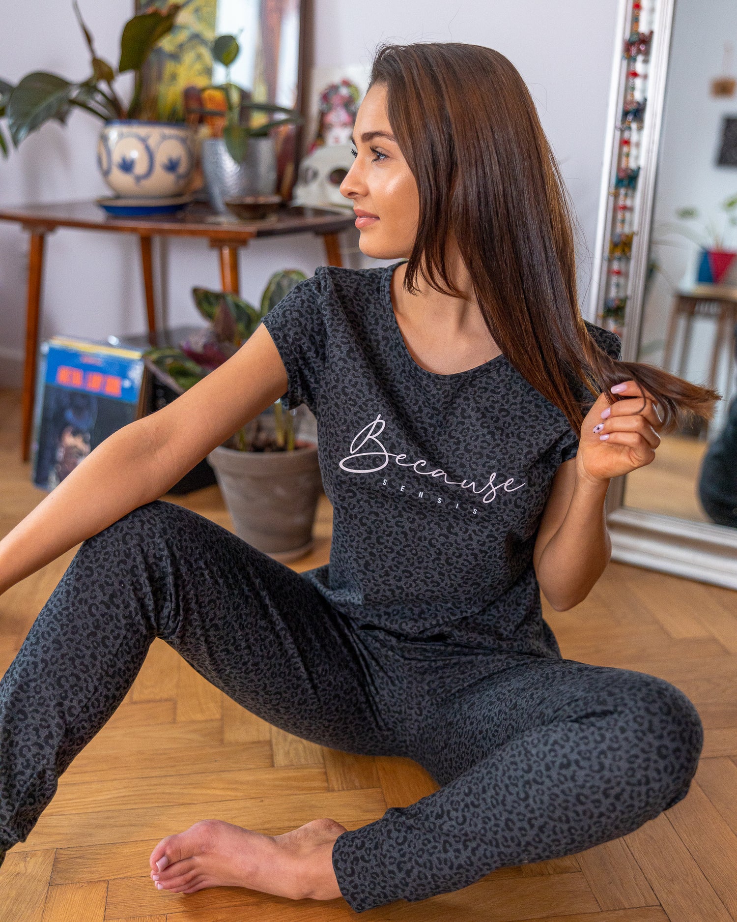 A Brunette female sitting on hardwood floor wearing Two piece outfit set  Cotton-Blend Short Sleeve Top  Leopard Print Pattern  Soft Casual T-shirt  Long Pant Jogger  Cuff Ankles  Adjustable Satin Bow Tie  Sustainable pyjama set  Eco-conscious lounge Wear 