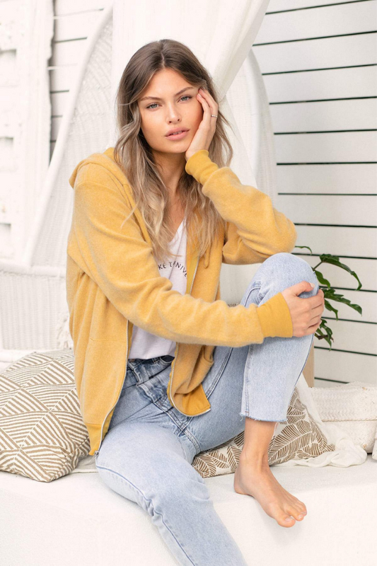 Bailage Haired Caucasian female wearing a Zip-Up Cuffed Long Sleeved Polyester Mixed Suede Fleece Pullover Cosy Soft Exterior Feel Two Side Pockets Casual Hooded Sweatshirt Jacket in Mustard paired with a v-neck white graphic tee with light washed denim skinny jeans
