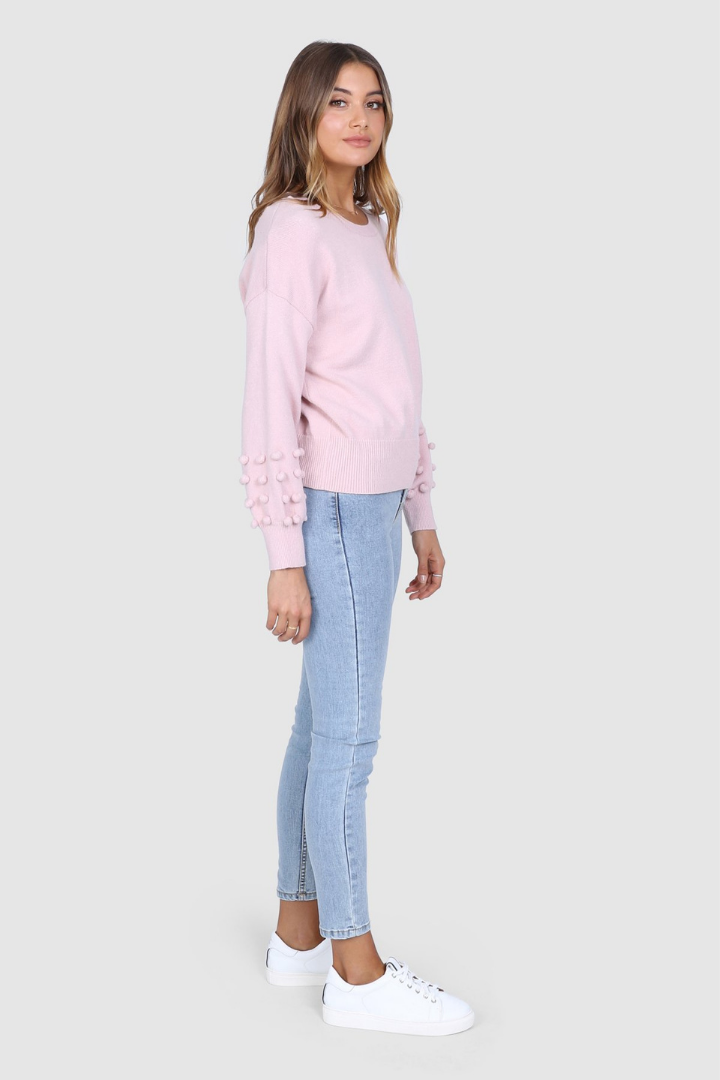 Bailage Haired Caucasian Female wearing Soft Knit Sweater  Cozy Pullover  Flattering Scoop Neckline  Balloon Long Sleeves  Lightweight  Pom Pom Detailed Sleeves  Ribbed Hemline and Cuffs  paired with high waisted light washed skinny jeans and white sneakers