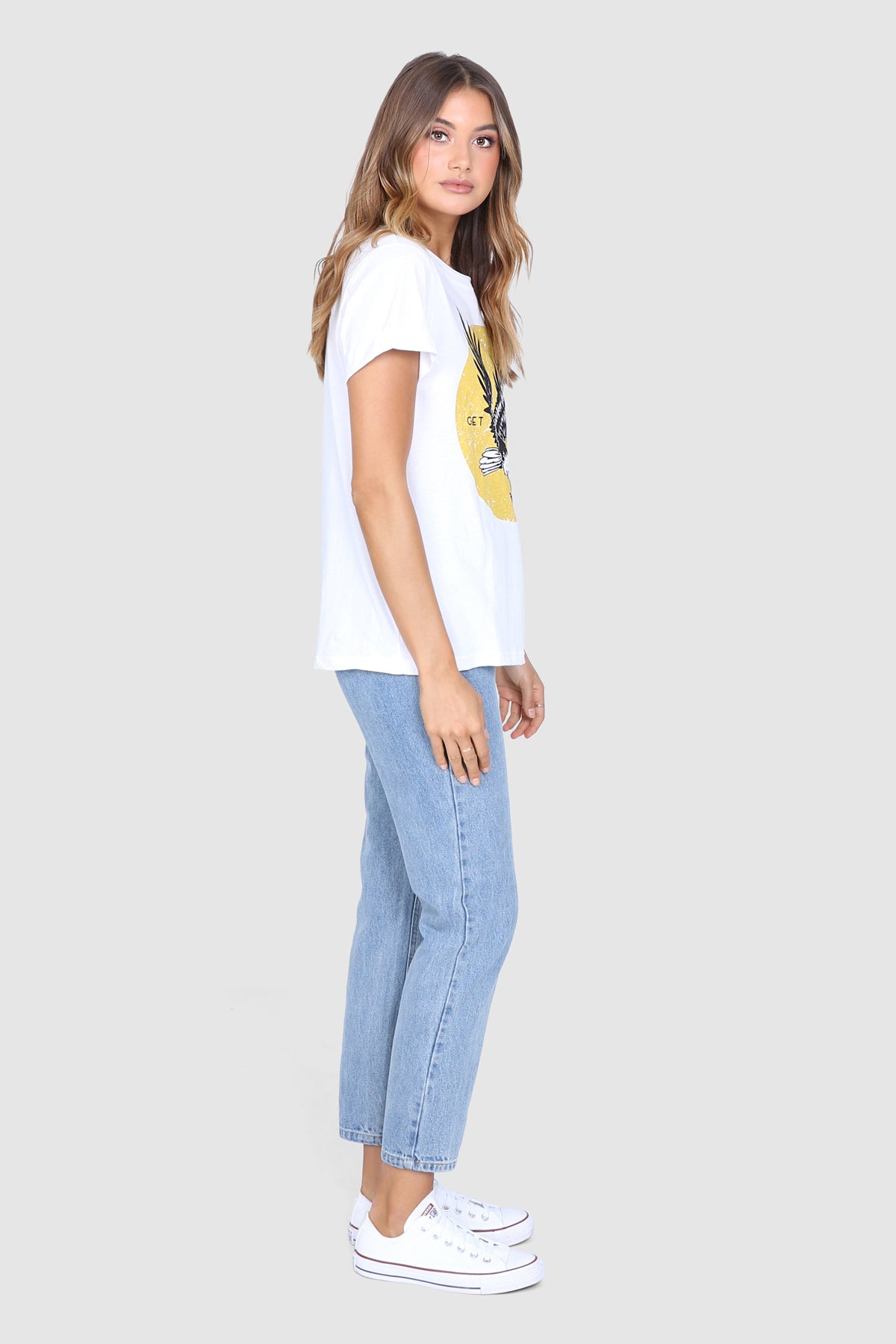 Bailage Haired Caucasian Female wearing aVintage Casual Eagle Graphic Tee Cotton Short Sleeved T-Shirt Relaxed Fit Round Neck Top paired with high waisted light washed mom jeans and white converse