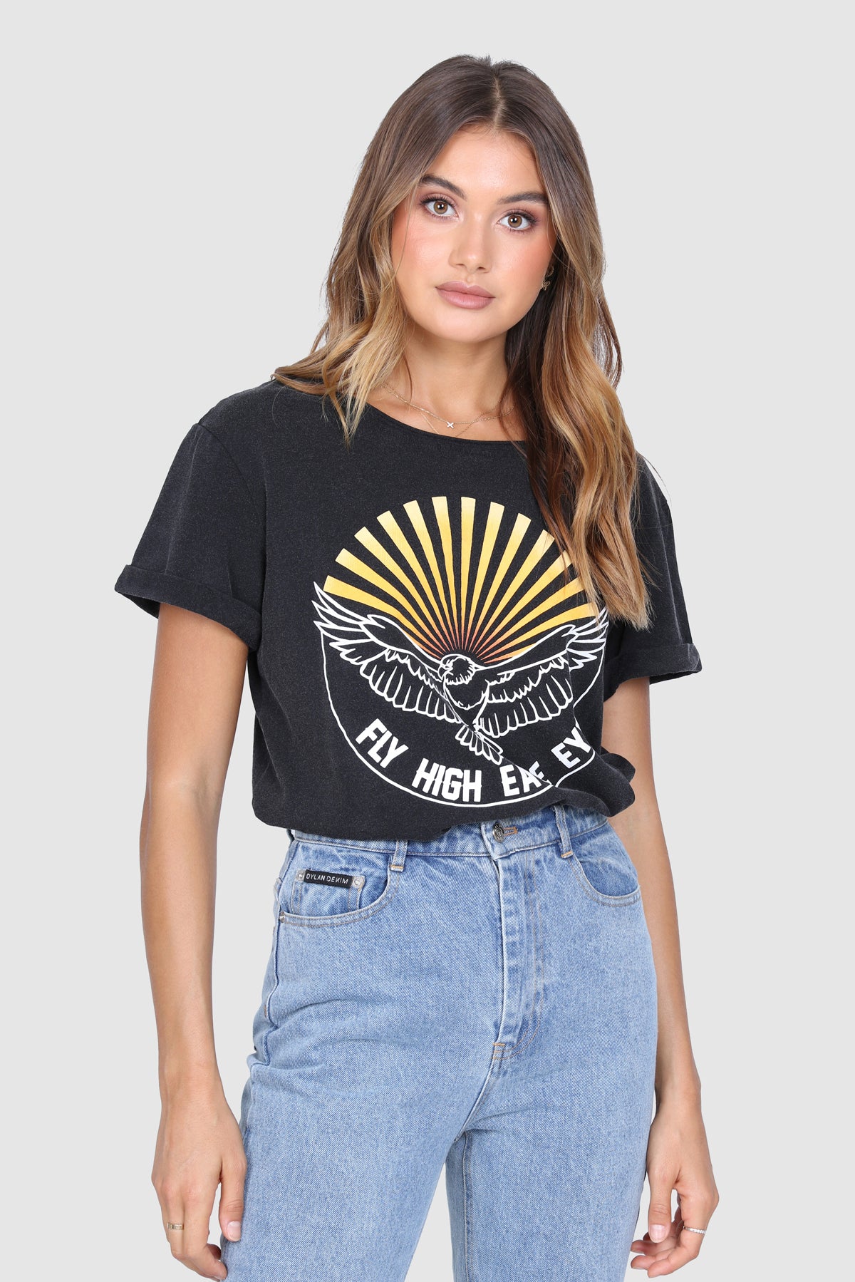 Bailage Curled Haired Caucasian female wearing Vintage  Cotton Casual  Graphic Tee  Short Sleeved T-Shirt  Relaxed Fit  Round Neck  70's vibe paired with high waisted light washed denim jeans and white converse 