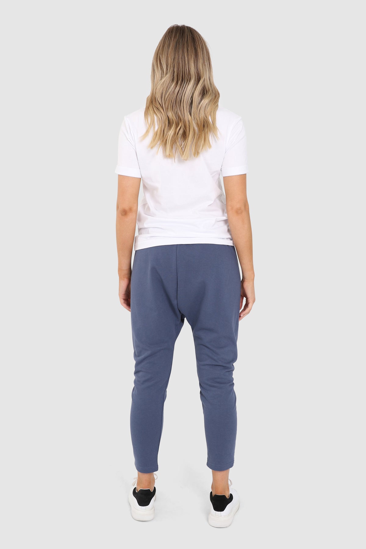 Tall Blonde Caucasian female wearing Adjustable Drawstring Drop Crotch pants Long Cotton-Blend Joggers Two Front Deep Pockets Casual Loungewear paired with graphic white t-shirt and white sneakers