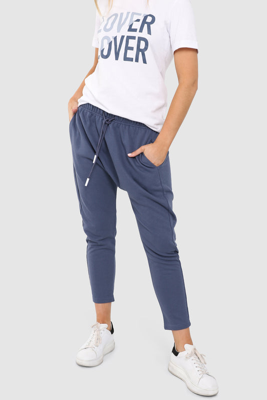 Tall Blonde Caucasian female wearing Adjustable Drawstring Drop Crotch pants Long Cotton-Blend Joggers Two Front Deep Pockets Casual Loungewear paired with graphic white t-shirt and white sneakers