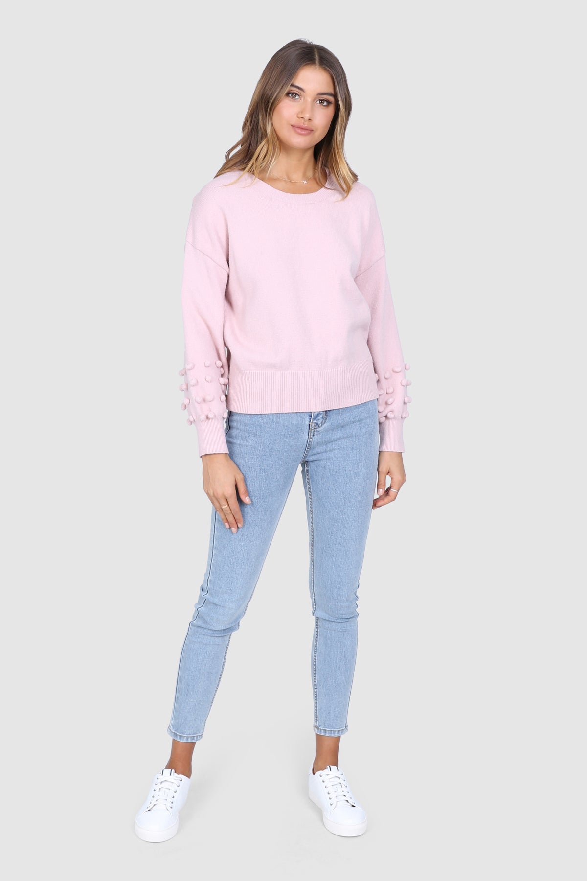 Bailage Haired Caucasian Female wearing Soft Knit Sweater  Cozy Pullover  Flattering Scoop Neckline  Balloon Long Sleeves  Lightweight  Pom Pom Detailed Sleeves  Ribbed Hemline and Cuffs  paired with high waisted light washed skinny jeans and white sneakers
