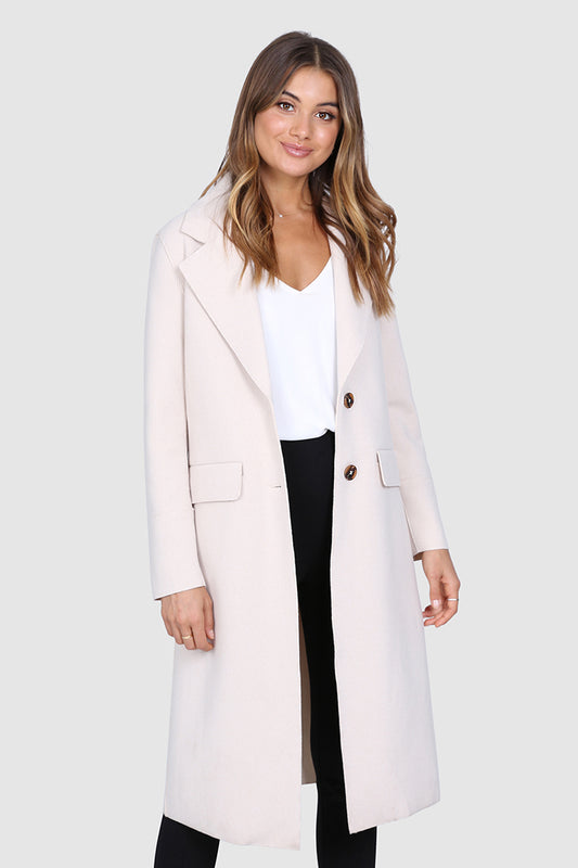Bailage Haired Caucasian female wearing Lapel Overcoat  Button Down Closure  Two-Front Pocket  Long Sleeved Coat  Open Front  Knee-Length Trench  Single Breasted Outerwear paired with v-neck white t-shirt with high waisted black trousers