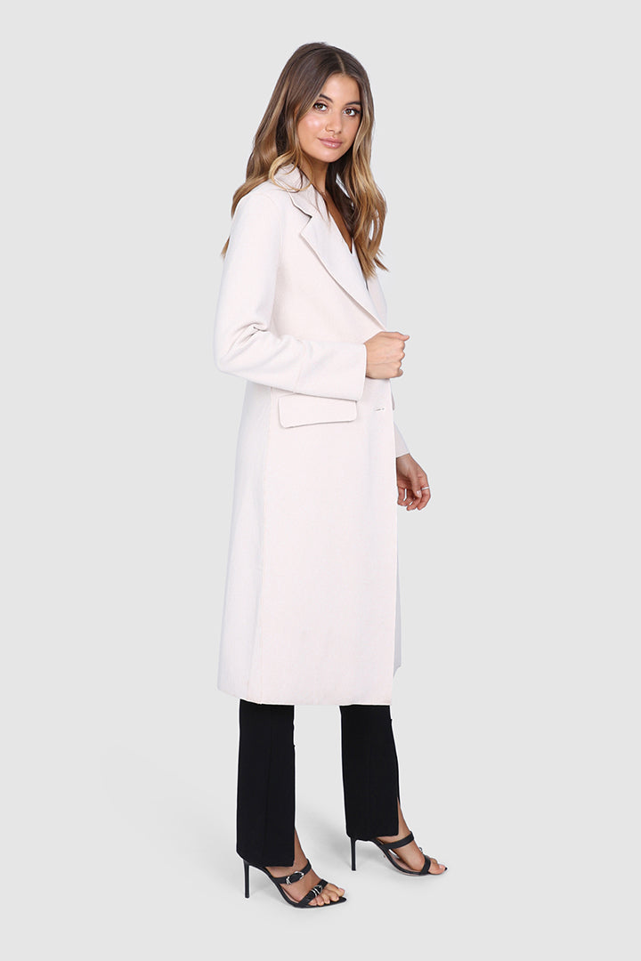 Bailage Haired Caucasian female wearing Lapel Overcoat  Button Down Closure  Two-Front Pocket  Long Sleeved Coat  Open Front  Knee-Length Trench  Single Breasted Outerwear paired with v-neck white t-shirt with high waisted black trousers and black open toed strapped stilettoed