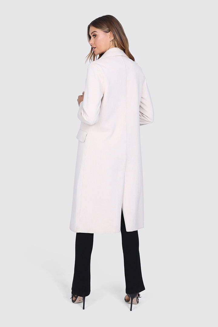 Bailage Haired Caucasian female wearing Lapel Overcoat Button Down Closure Two-Front Pocket Long Sleeved Coat Open Front Knee-Length Trench Single Breasted Outerwear paired with v-neck white t-shirt with high waisted black trousers and black open toed strapped stilettoed
