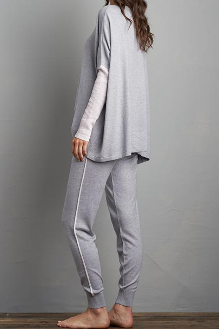 Brunette Curled Haired Caucasian Female wearing Relax Fit  Draped Shoulder  Cuffed Long Sleeves  Round Neck Jumper  Lightweight  Flowy Material  Batwing Sleeves  Slightly Boxy Fit Lounge Sweater Paired with matching long cuffed grey joggers with adjustable drawstrings