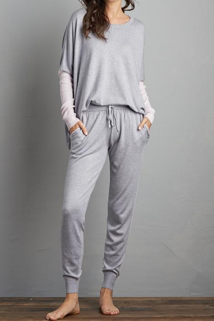 Brunette Curled Haired Caucasian Female wearing Relax Fit  Draped Shoulder  Cuffed Long Sleeves  Round Neck Jumper  Lightweight  Flowy Material  Batwing Sleeves  Slightly Boxy Fit Lounge Sweater Paired with matching long cuffed grey joggers with adjustable drawstrings