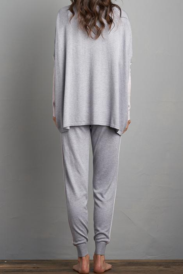 Brunette Curled Haired Caucasian Female wearing Relax Fit  Draped Shoulder  Cuffed Long Sleeves  Round Neck Jumper  Lightweight  Flowy Material  Batwing Sleeves  Slightly Boxy Fit Lounge Sweater Paired with matching long cuffed grey joggers with adjustable drawstrings