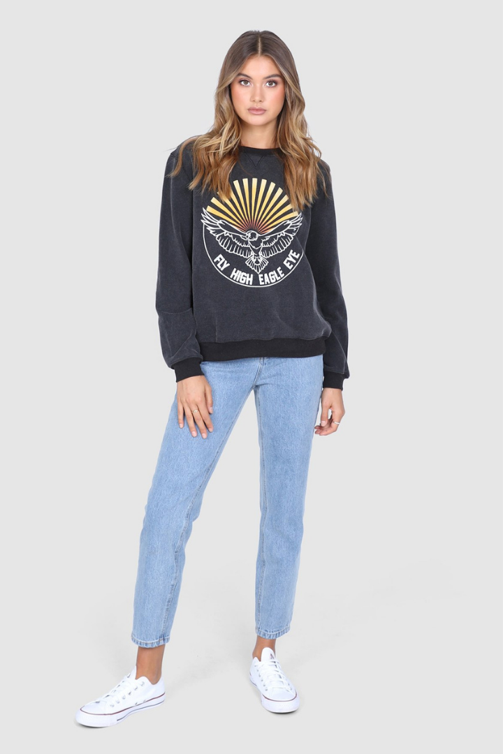 Bailage haired Caucasian Female wearing a  Vintage  Cotton Crew Neck  Round Neck  Eagle Graphic  Cuffed Long Sleeves  Relaxed Fit  Smoky Pullover paired with light washed mom jeans and white converse