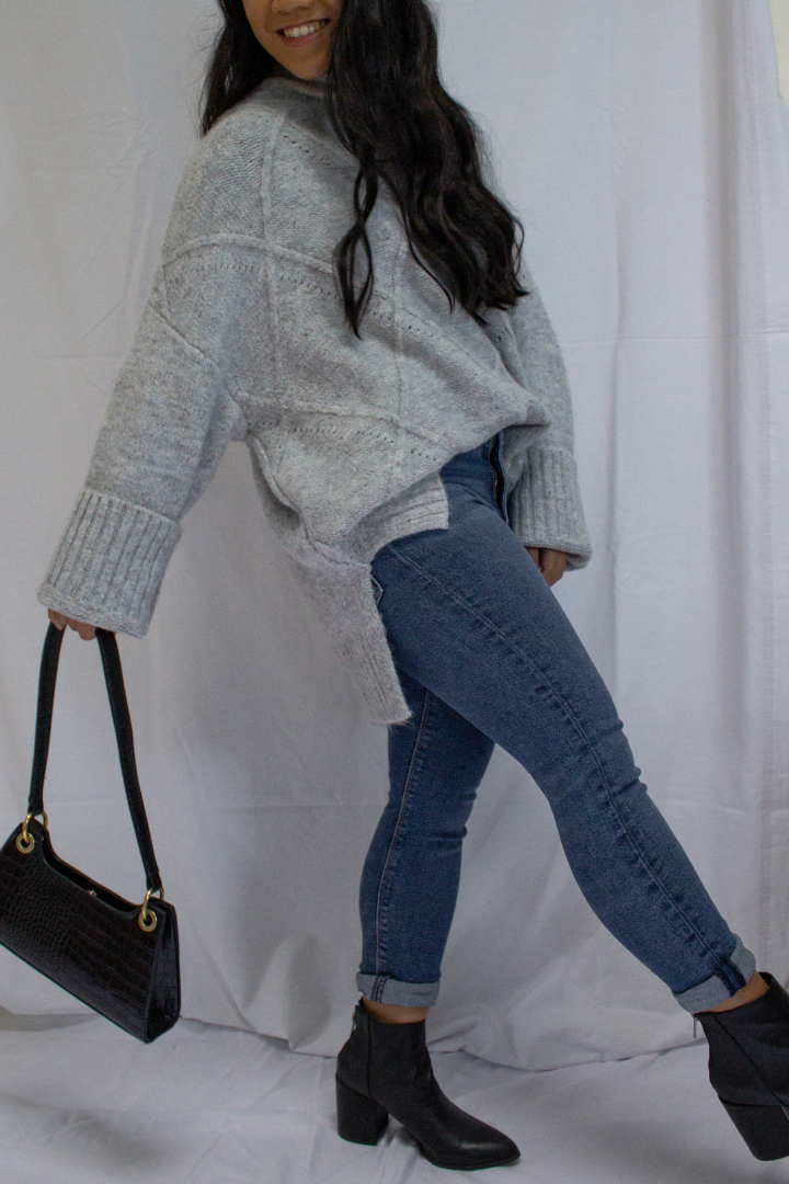 A Black Haired Asian Canadian wearing a Casual  Chunky  Turtleneck  Knit  Batwing  Long Sleeve  Ribbed Cuffs  Comfy  Stylish  Dropped Shoulder  Sweater Pullover paired with high waisted dark denim skinny jeans, ankle-high close top leather booties and faux croc leather hand bag in black