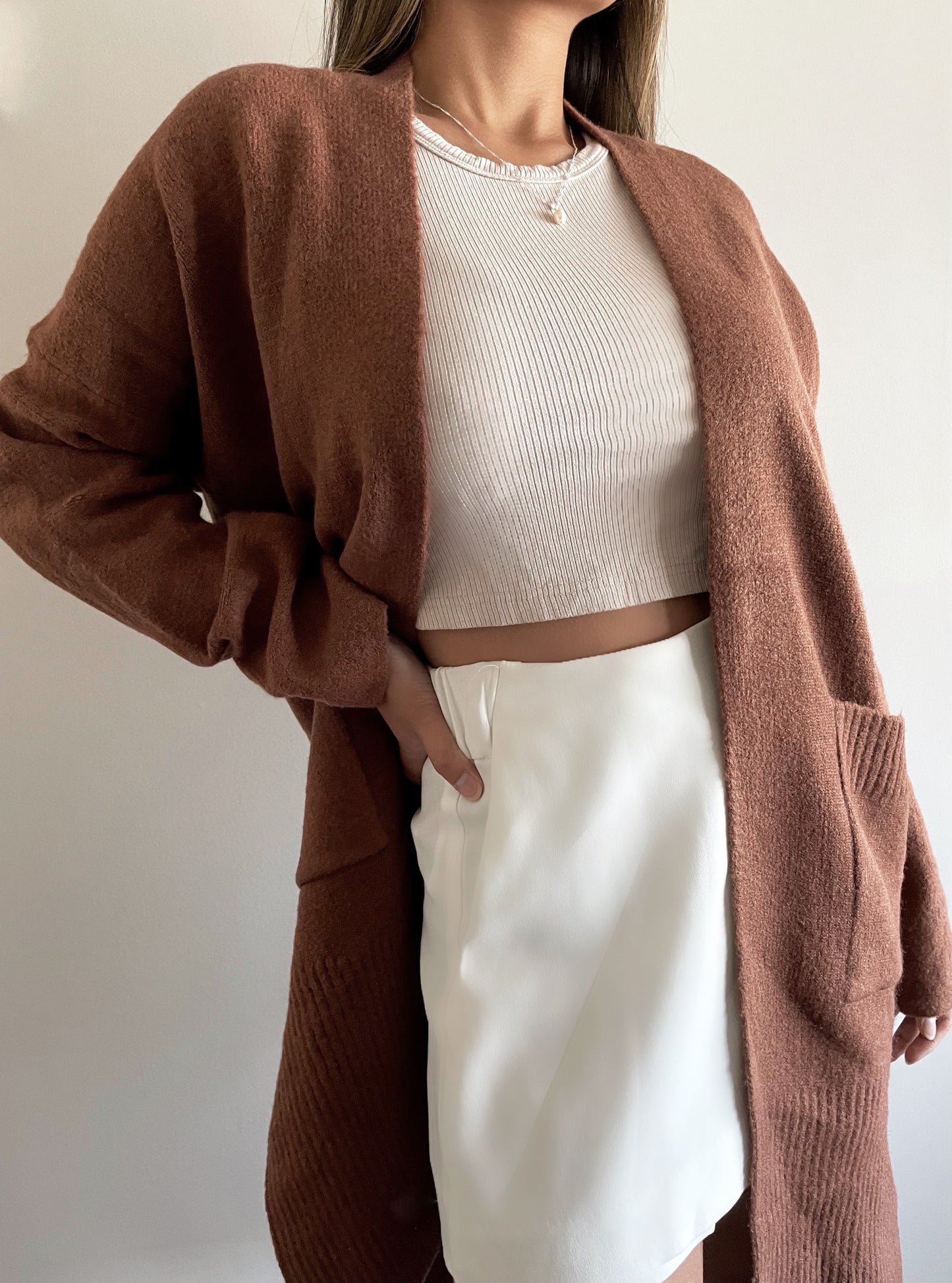 Asian Canadian female wearing wearing an Open Front Basic Versatile Dropped Shoulder Two Deep Side Pockets Two Side Split Slightly Oversized Ribbed Hemline And Cuffs Long Sleeved Cardigan in Rich Dark Chocolate paired with high scoop neck ribbed tank and white high waisted skirt 