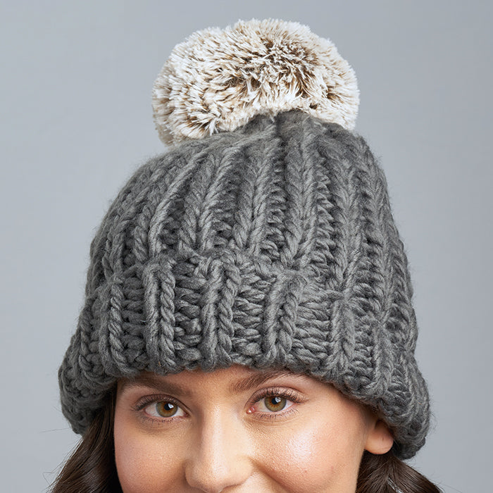 Brunette Caucasian Female wearing Chunky Cable Knit Faux Fur Pom Pom Ribbed Detailed Timeless Winter Accessory Stretchy Toque Easy Slip On Beanie in Charcoal