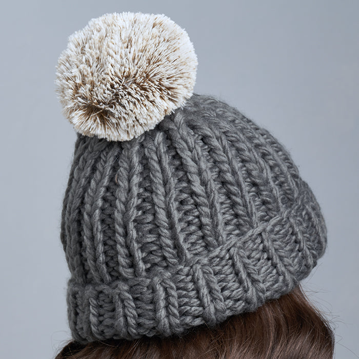 Brunette Caucasian Female wearing Chunky Cable Knit Faux Fur Pom Pom Ribbed Detailed Timeless Winter Accessory Stretchy Toque Easy Slip On Beanie in Charcoal