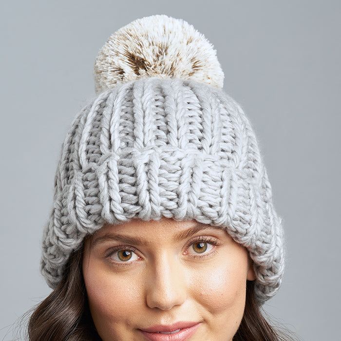 Brunette Caucasian Female wearing Chunky Cable Knit Faux Fur Pom Pom Ribbed Detailed Timeless Winter Accessory Stretchy Toque Easy Slip On Beanie in Grey