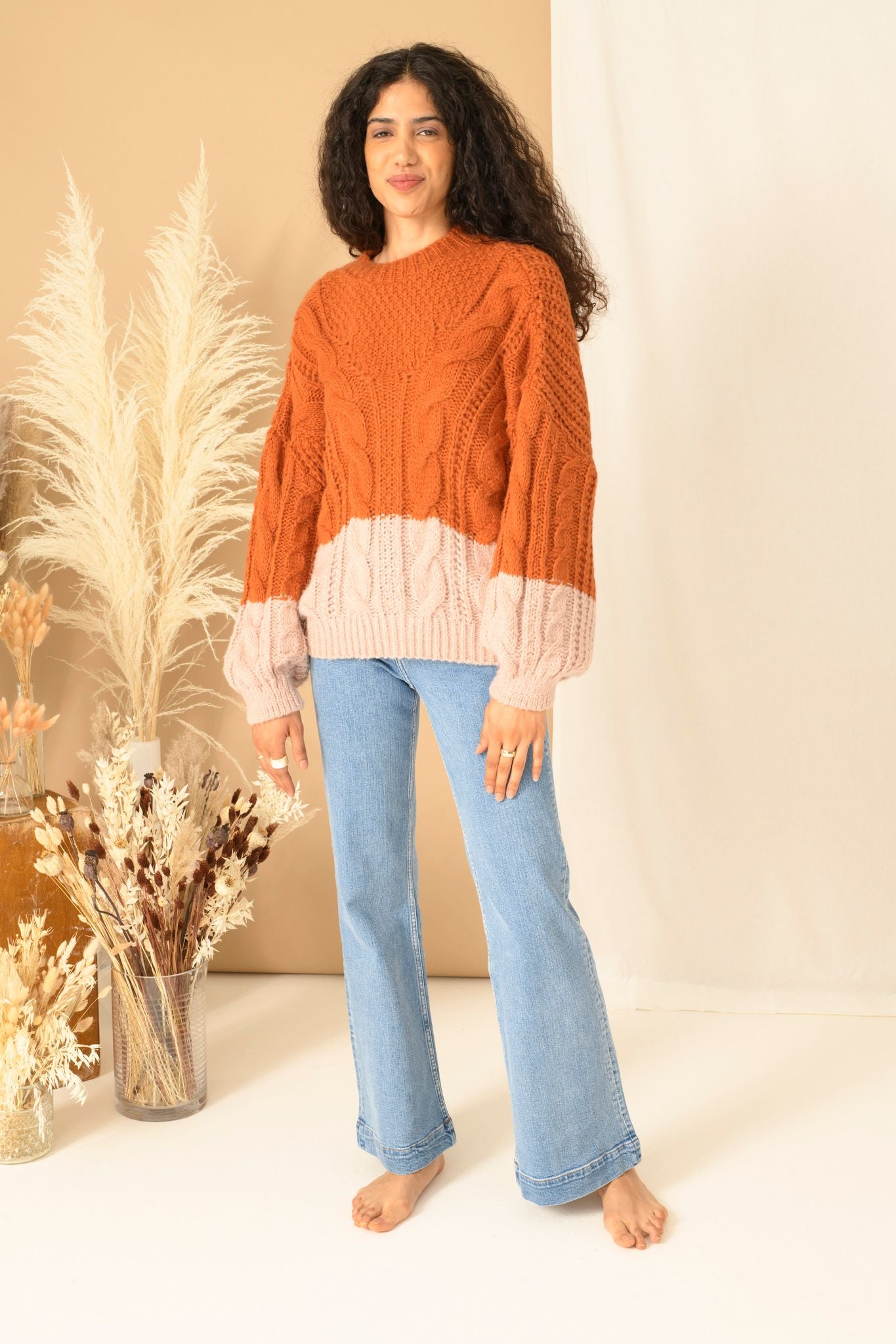 Brunette Curled Haired Caucasian female wearing Cable jumper Knitwear  Chunky  Balloon Sleeve  Cosy  Color Block  Turtleneck  Casual  Basic Long Sleeve  Pullover Sweater paired with high waisted flared light washed jeans 