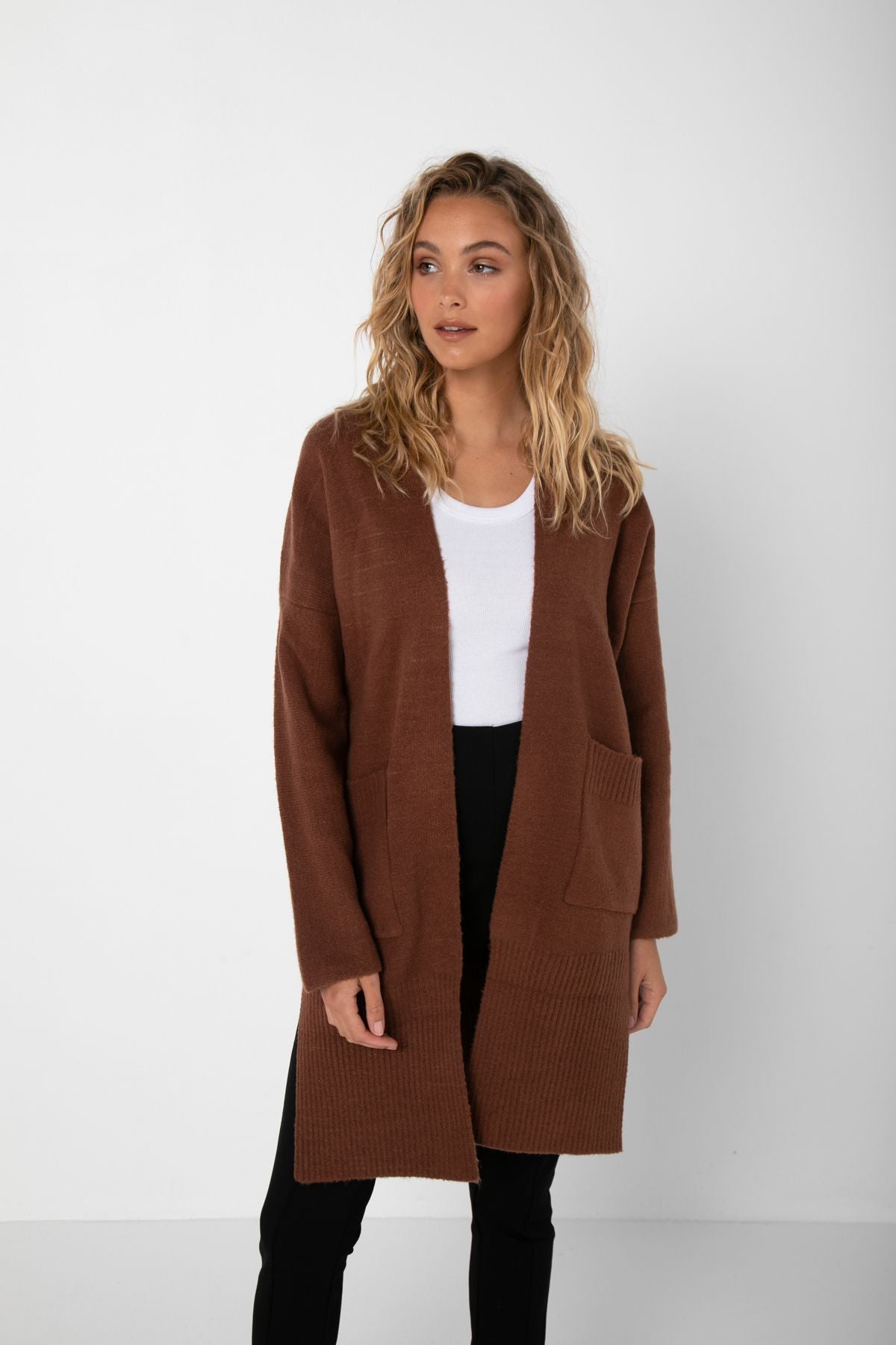 Curled Bailage Caucasian Female wearing an Open Front  Basic  Versatile  Dropped Shoulder  Two Deep Side Pockets  Two Side Split  Slightly Oversized  Ribbed Hemline And Cuffs  Long Sleeved Cardigan  in Rich Dark Chocolate paired with high waisted stretchy black denim skinny jeans 