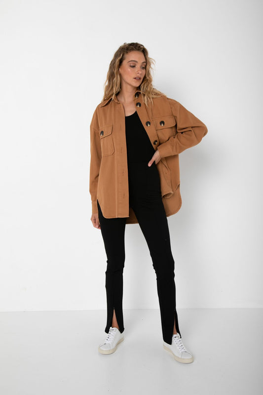 Curled Bailage Hair Caucasian Female wearing Long Sleeve Buttoned Down Top  Lightweight  Boyfriend Relaxed Fit Jacket Blouse Stylish Shacket  Timeless Autumn and Winter Accessory  Two Front Buttoned Pockets  Side Slits in Tan paired with scoop neck black tee and Black high waisted stretchy long front slit pants and white sneakers